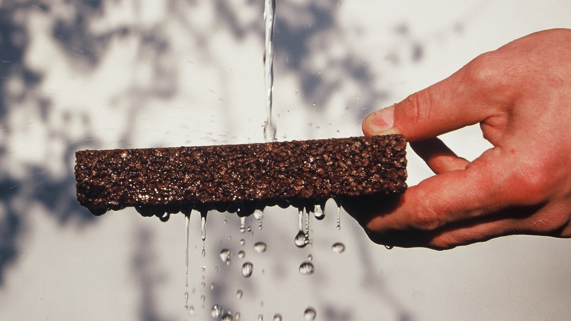 Hand hält ein Stück Terraway®-Belag unter einen Wasserstrahl